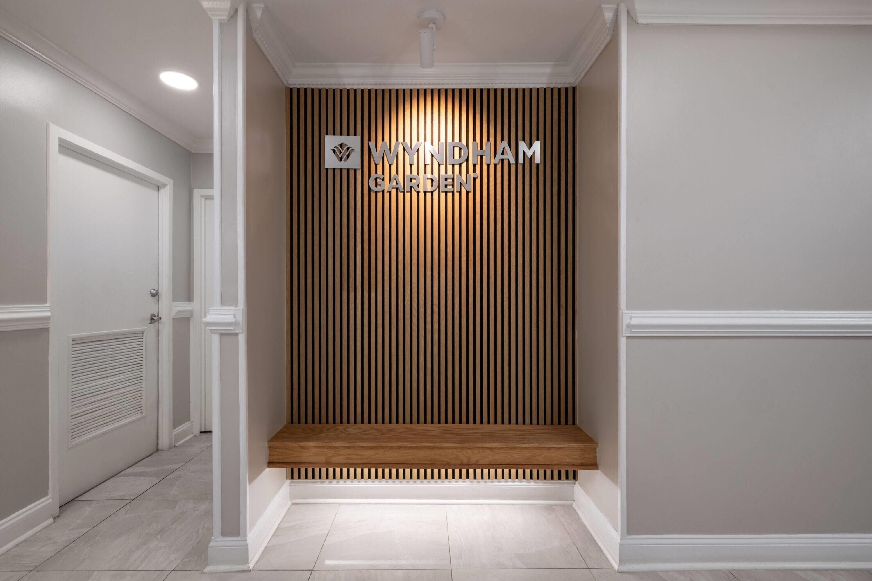 A hallway with a wooden panel wall, a bench, and a door on the left.