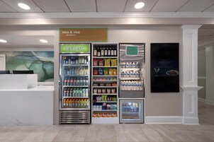 Un área de refrigerios con un letrero 'nice & vice market', un letrero 'REFRESH' sobre un enfriador de bebidas y un letrero que dice 'please visit APPLEGATE'.