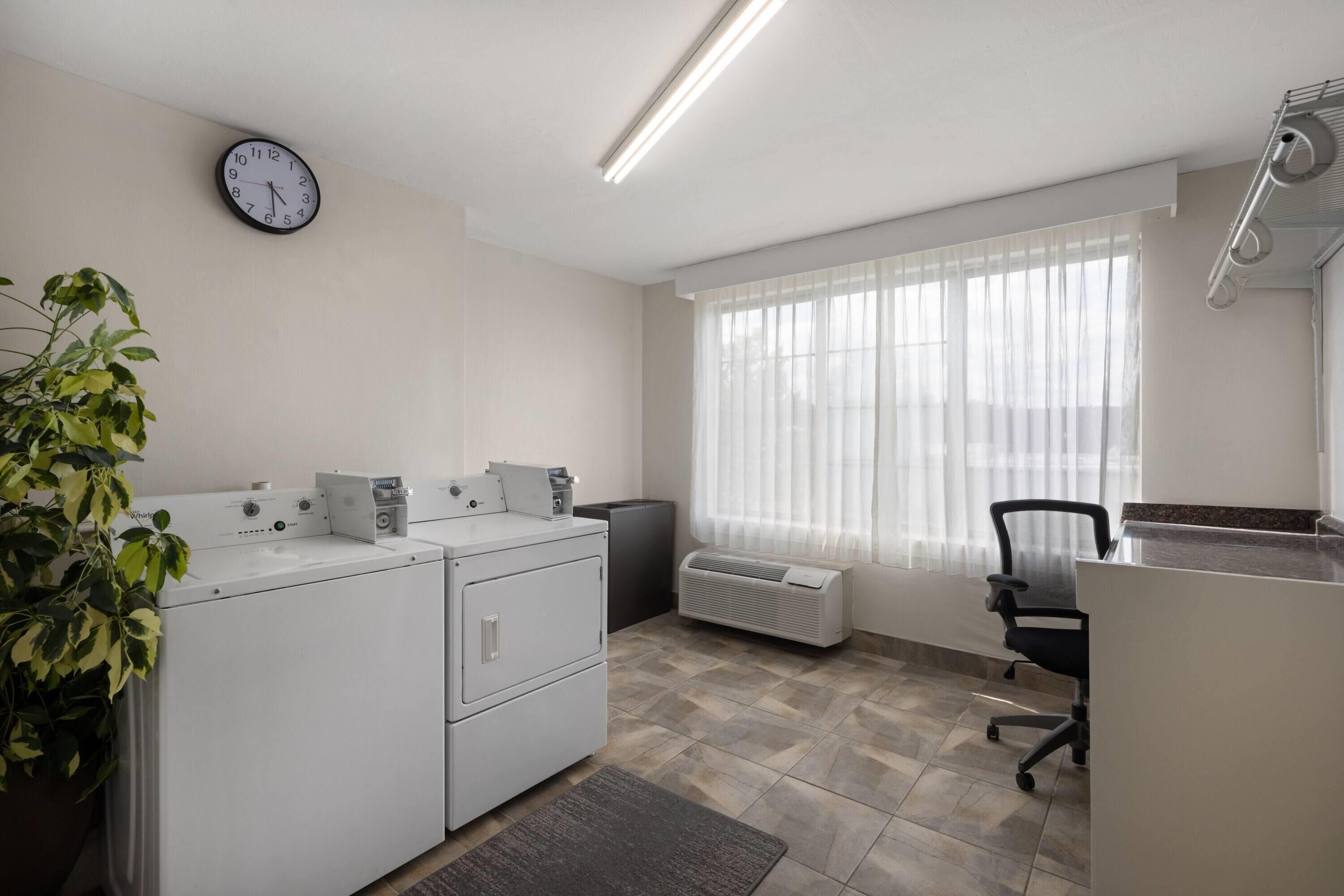 A clean, modern office space with a washing machine, a radiator, a desk with a chair, and a clock on the wall.
