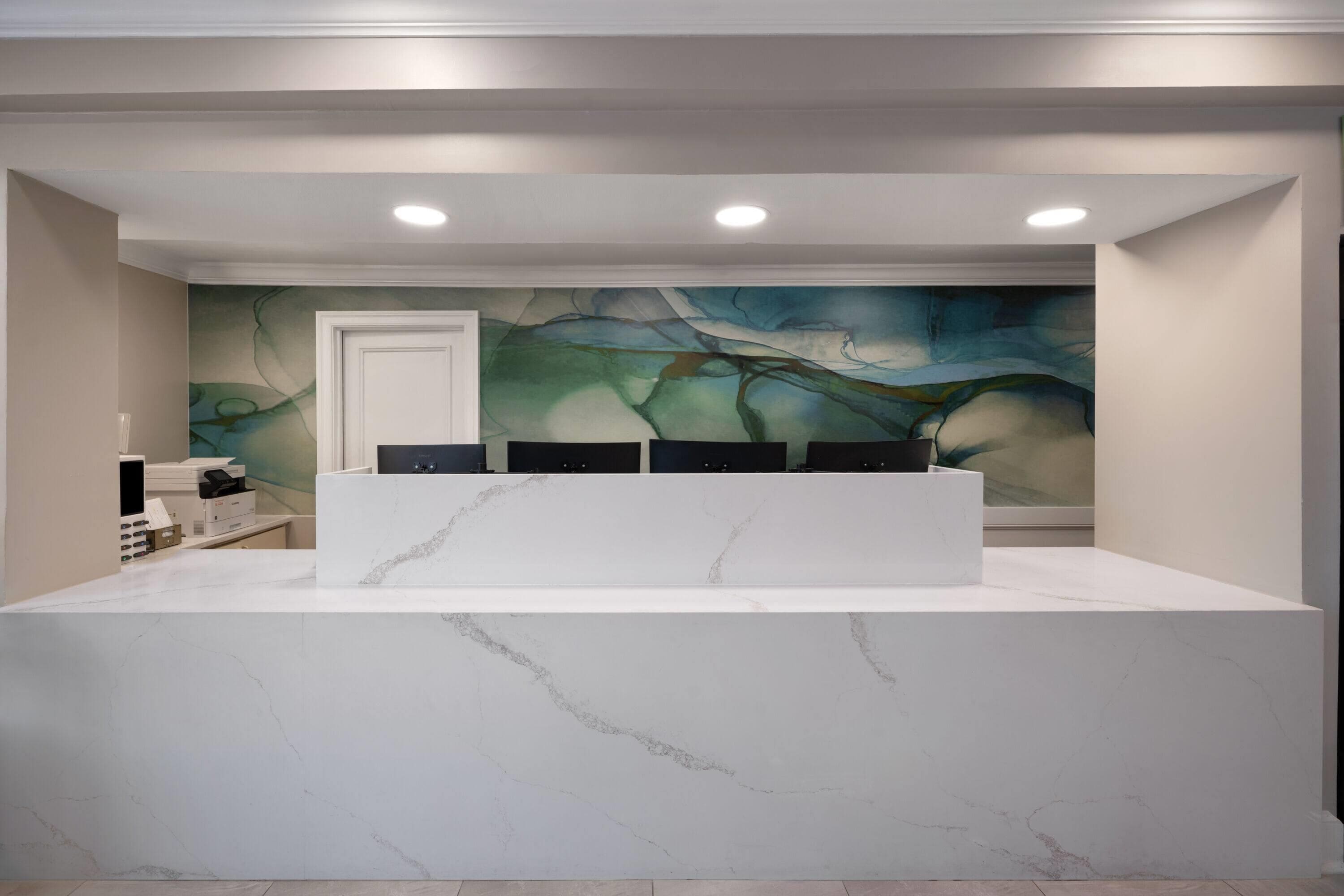 Uma área de recepção com balcão de mármore, um mural na parede e uma porta.