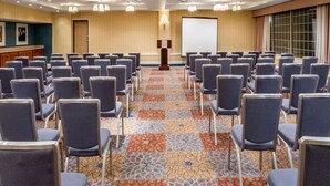 Un salón de conferencias con filas de sillas, un atril y una pantalla para proyector.