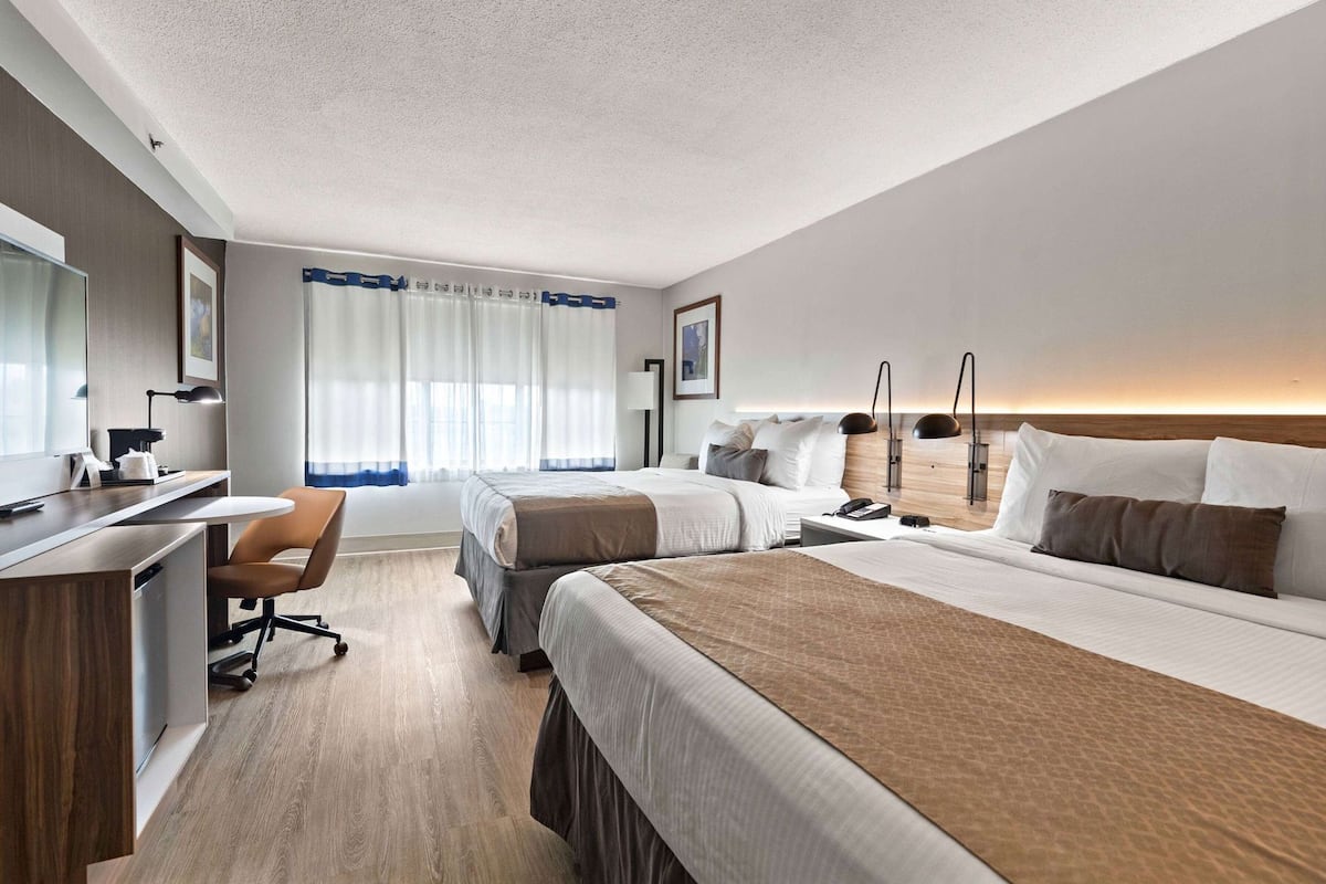 A hotel room with two beds, a desk, a chair, and a large window with curtains.