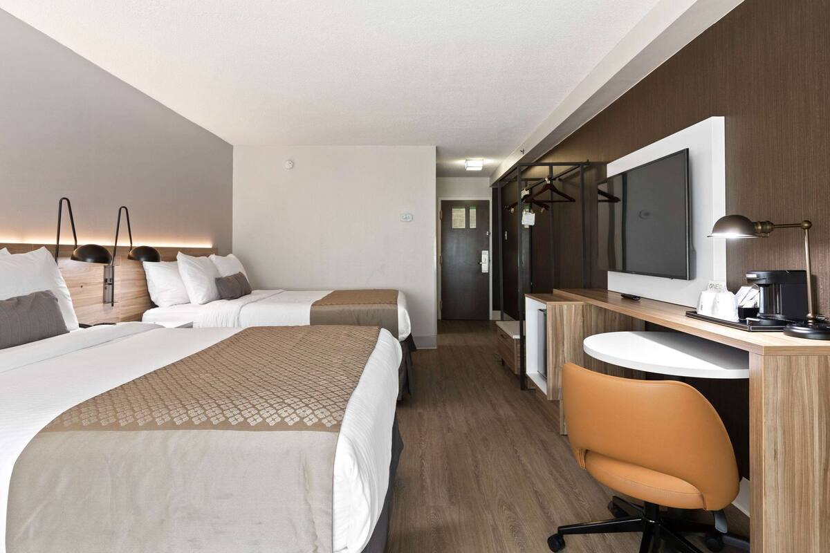 A hotel room with two beds, a desk with a chair, a TV, and a mirror.
