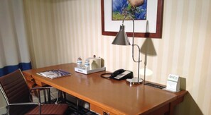 A hotel room with a wooden desk, a chair, a telephone, a lamp, a water bottle, a tissue box, and a framed picture on the wall. - Wyndham Garden Manassas (Manassas)