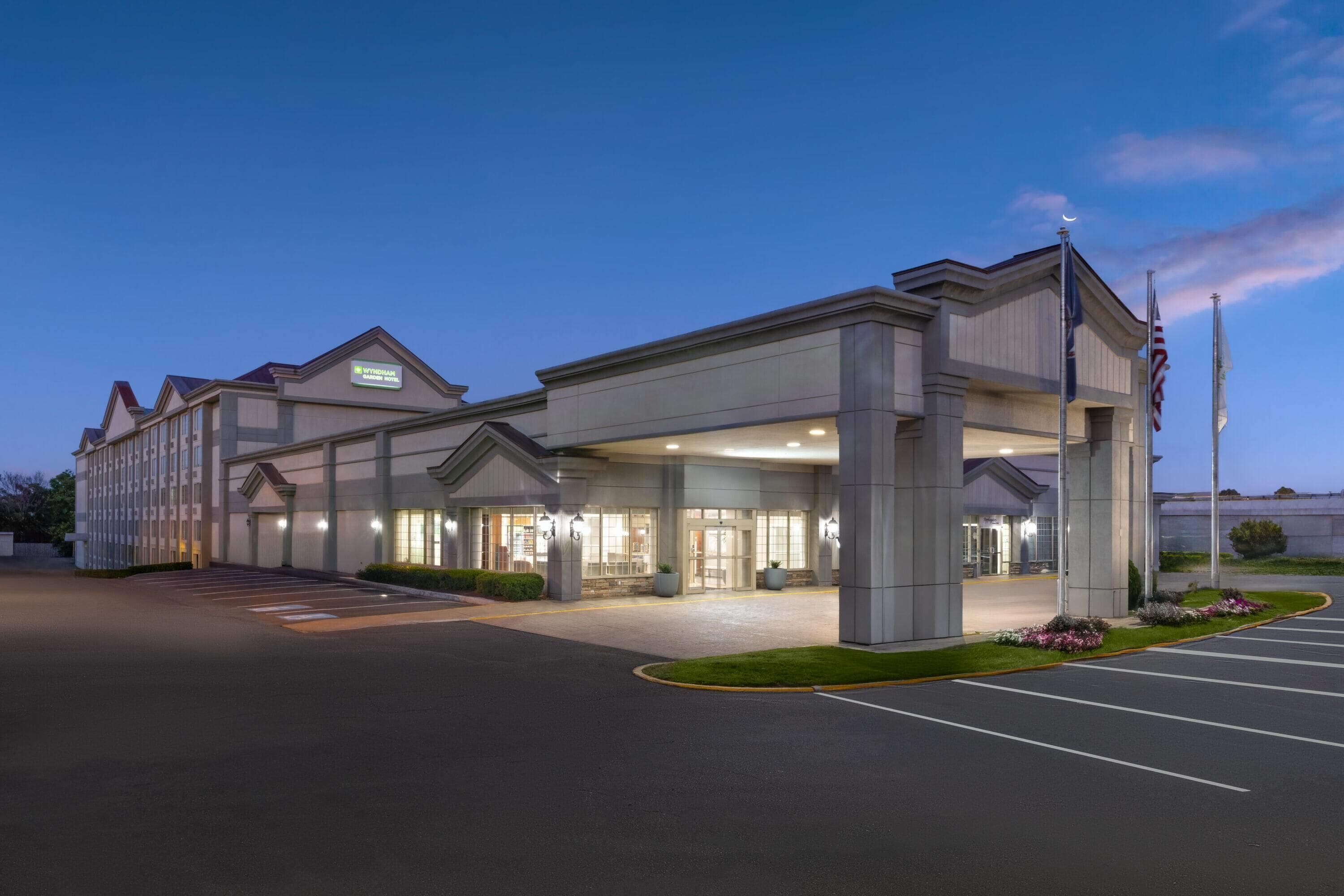 A hotel with a covered entrance, a parking lot, and a flagpole.