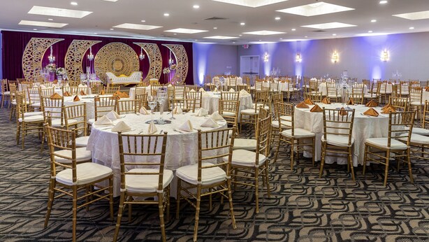 Un salón de banquetes con mesas redondas, sillas doradas y una alfombra estampada.