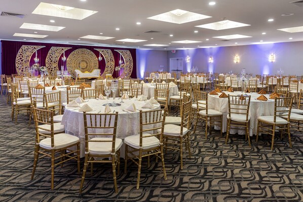 A banquet hall with round tables, gold chairs, and a patterned carpet. - Wyndham Garden Manassas (Manassas)