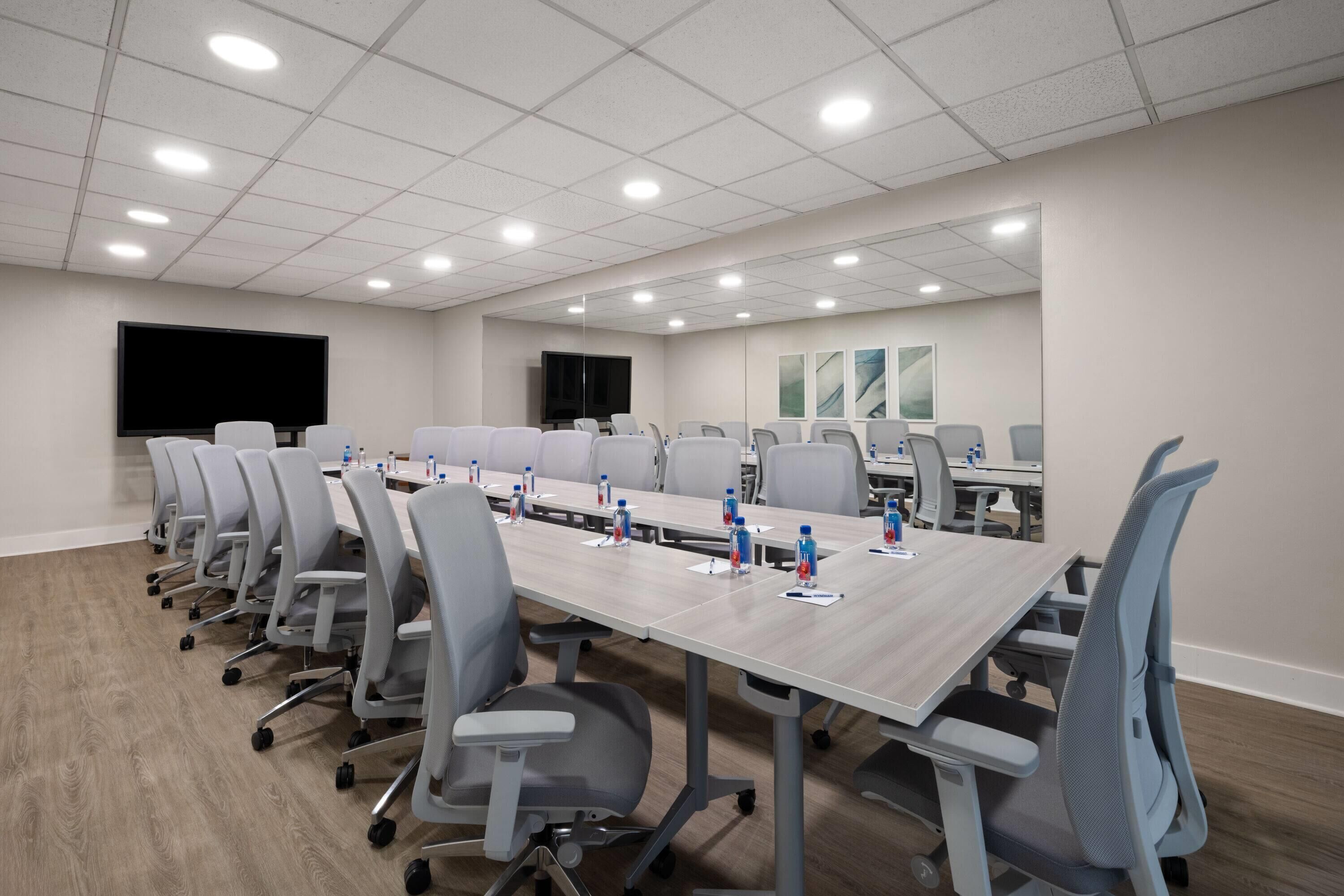 A conference room with a long table, multiple chairs, and a large screen.