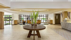 A spacious lobby with a round wooden table, two glass vases with flowers, and a reception desk. - Hilton Garden Inn Monterey (Monterey)