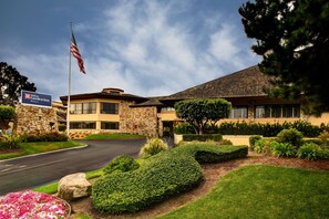 A hotel with a stone facade, a flag, and well-maintained landscaping. - Hilton Garden Inn Monterey (Monterey)