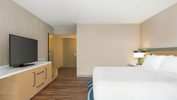 A hotel room with a bed, a TV on a wooden cabinet, a nightstand with a lamp, and a mirror on the wall.