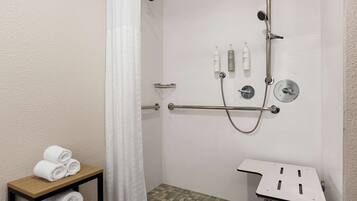 A shower area with a handheld showerhead, a wall-mounted faucet, and a grab bar. There are towels stacked on a shelf, and a shower caddy with toiletries.