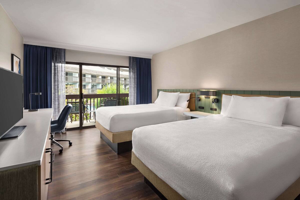 A hotel room with two beds, a desk, and a chair.