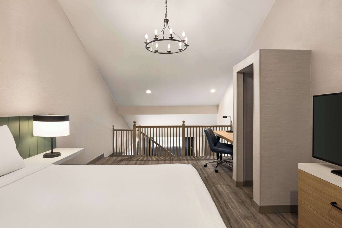 A hotel room with a bed, desk, chair, TV, and a staircase leading to an upper level.