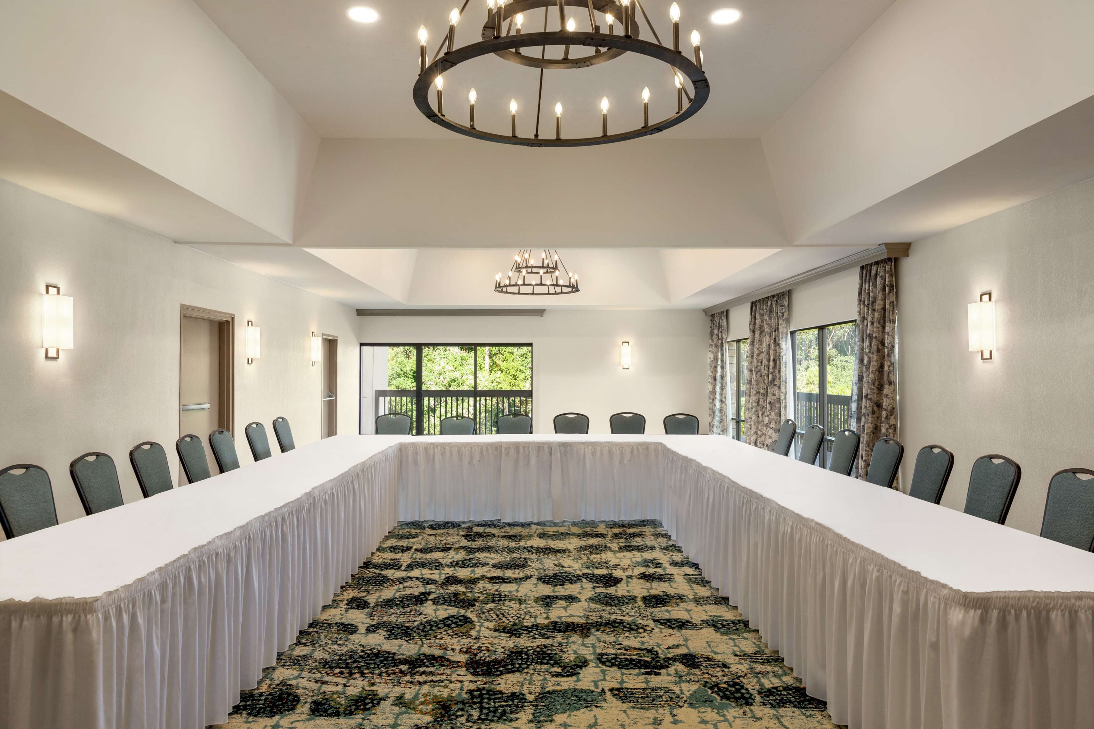 A conference room with a long table, chairs, a chandelier, wall sconces, and large windows.