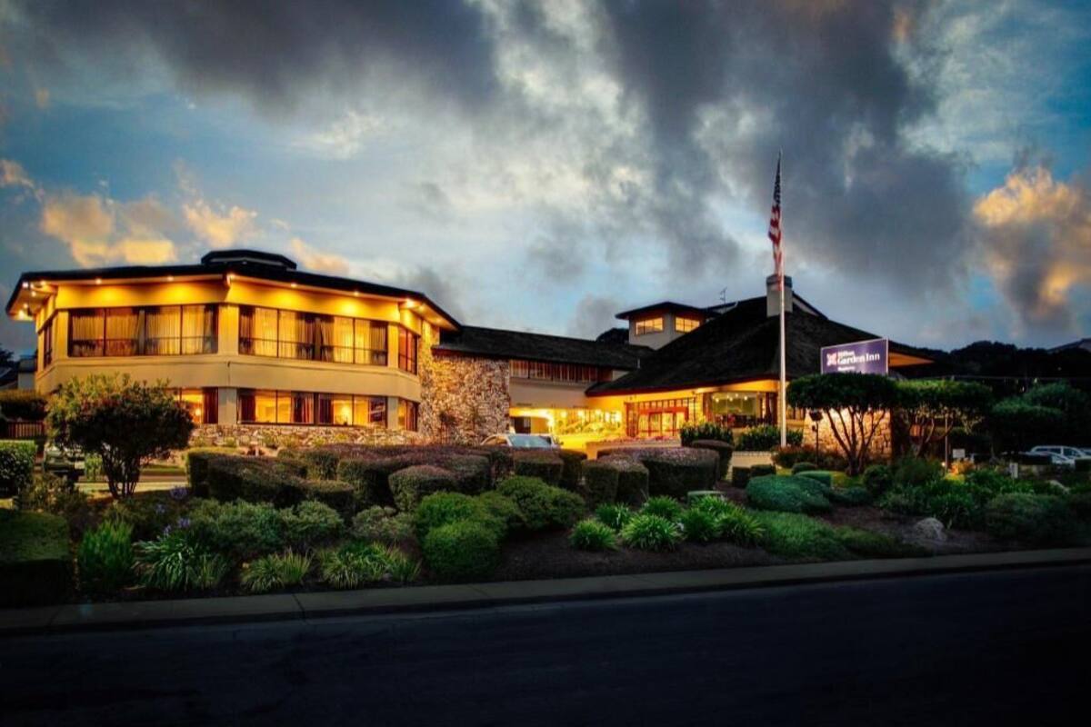 A hotel with a curved facade, a flagpole, and well-maintained landscaping.