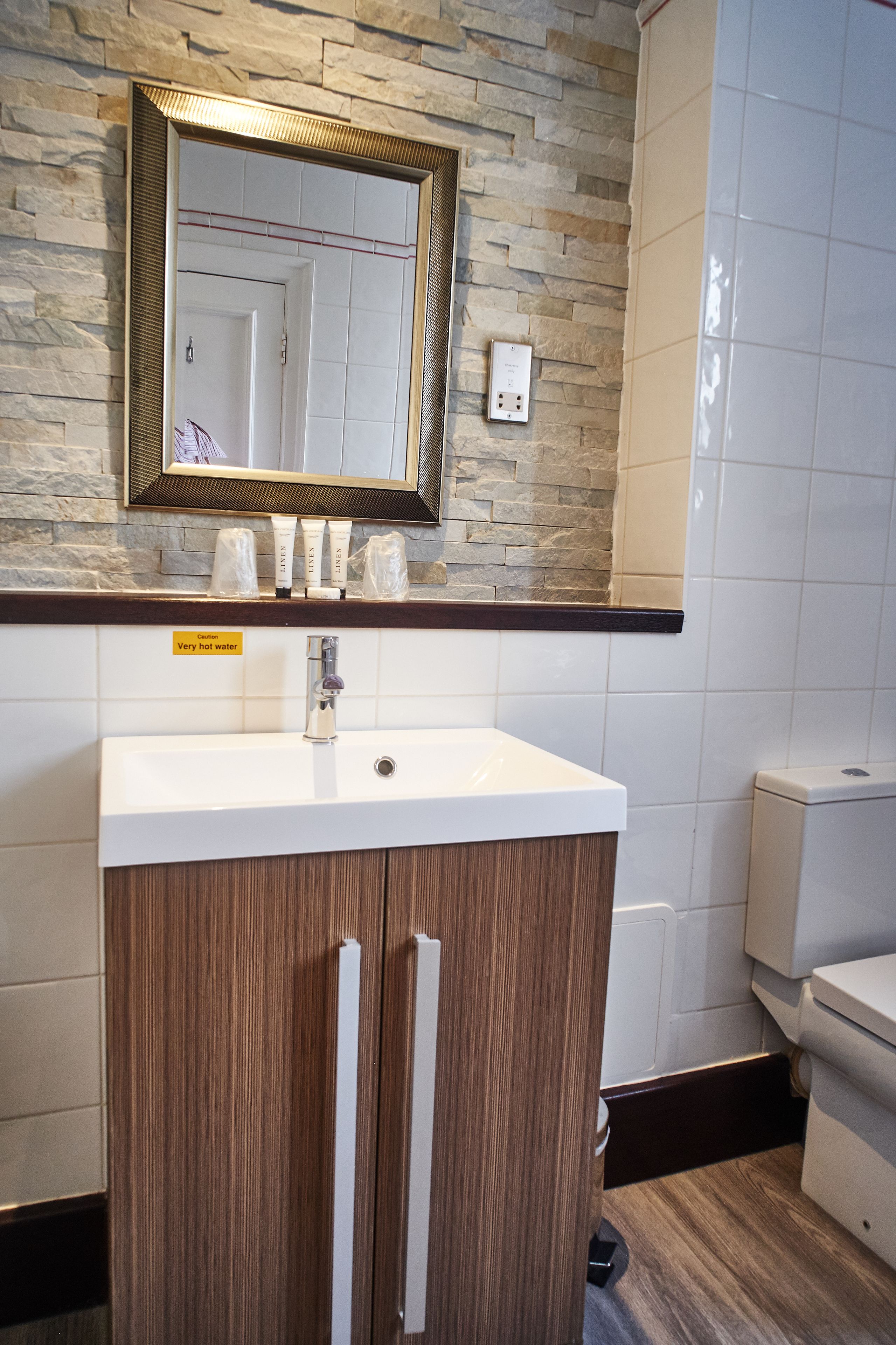 A bathroom with a stone wall, a white sink with a mirror above it, and toiletries on the counter.