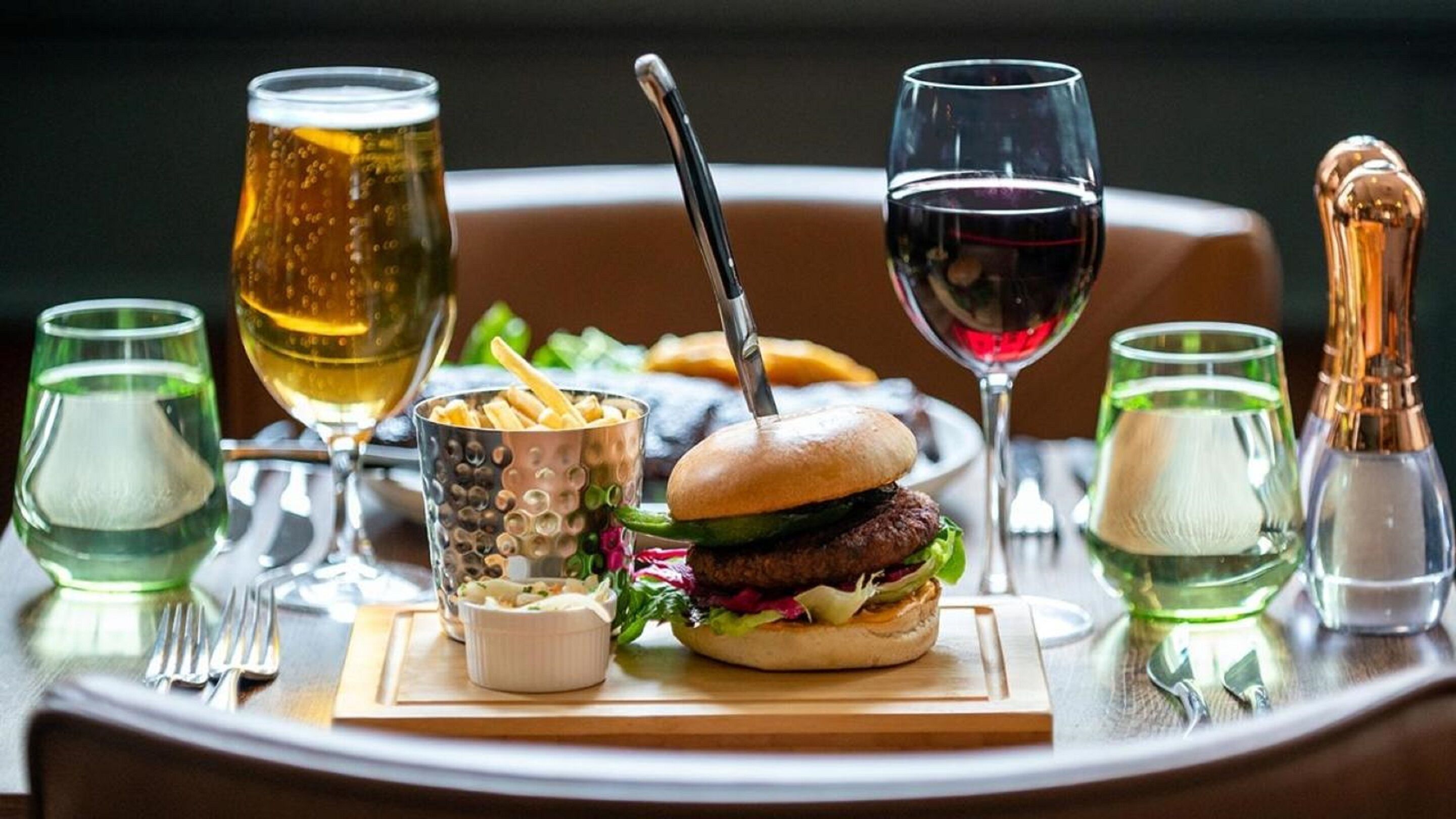 A dining table with a burger, glasses of beer and wine, and condiments.