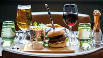 A dining table with a burger, glasses of beer and wine, and condiments.