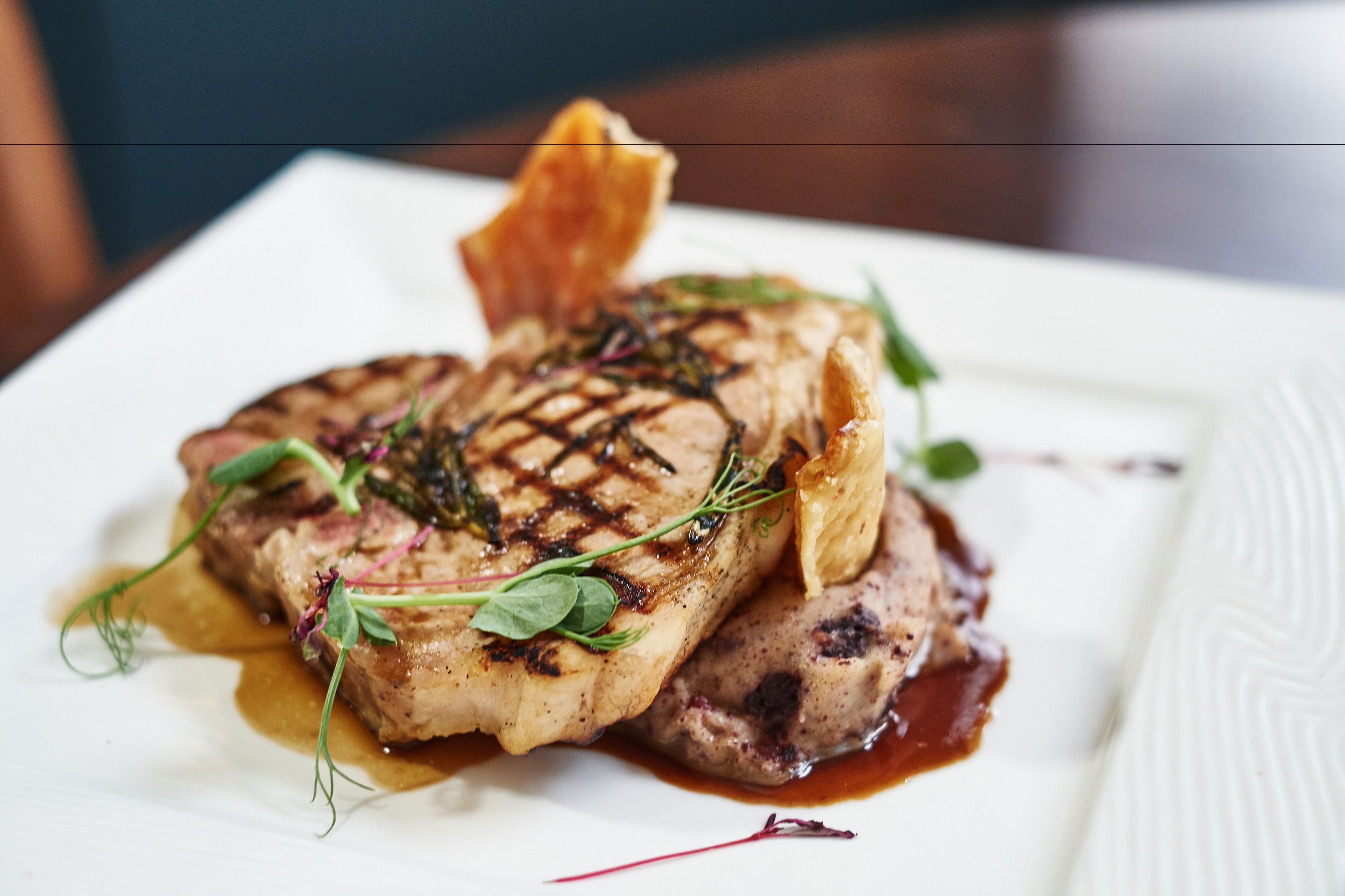 A plate of food with a grilled steak, a piece of fish, and a sauce.