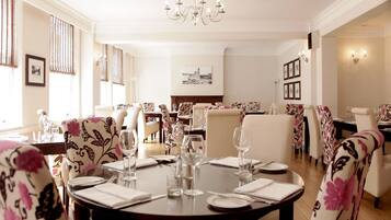 A dining area with round tables set for four, surrounded by floral-patterned chairs.