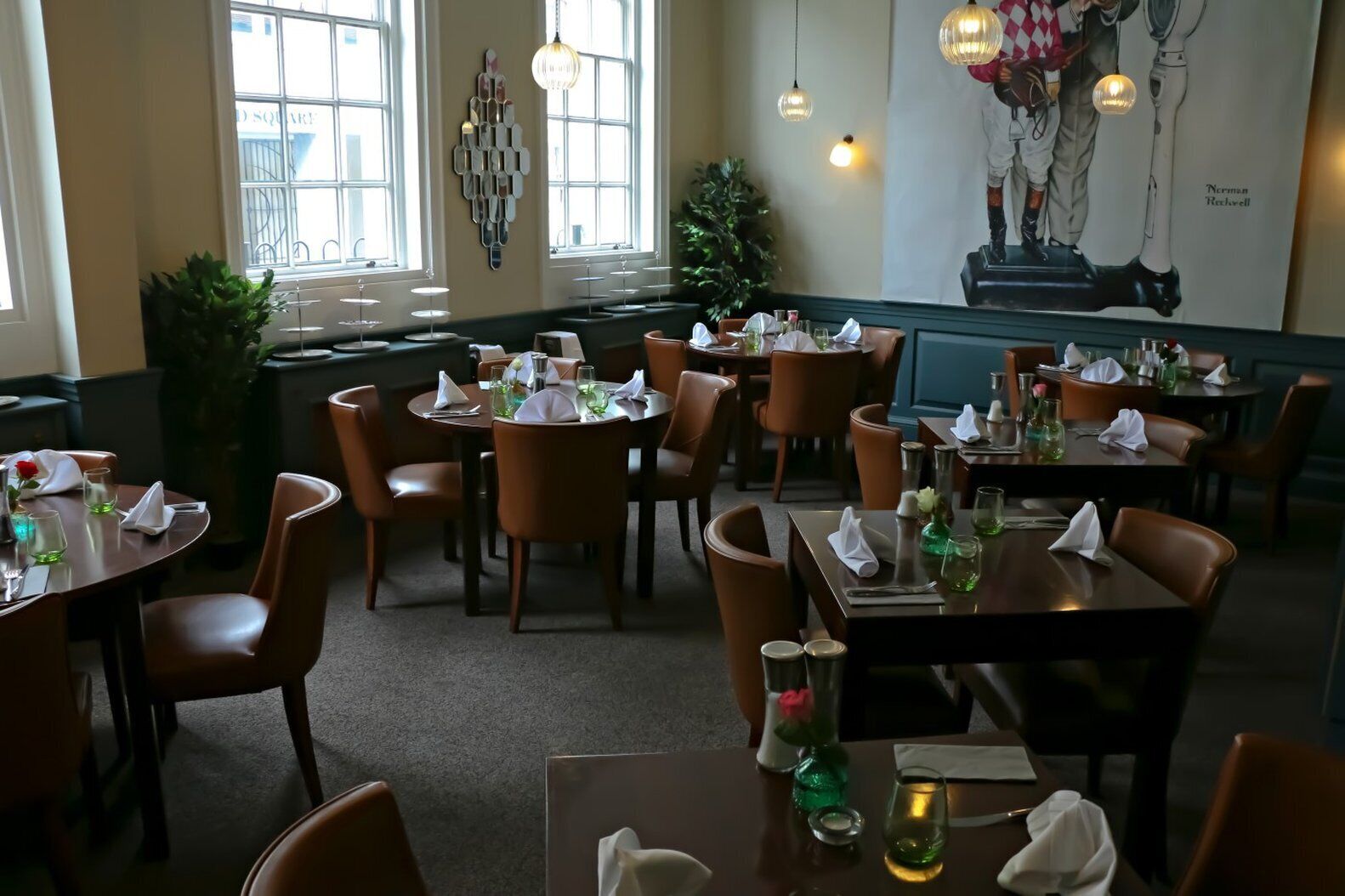 Un restaurante con mesas redondas, sillas de cuero marrón y un ventanal grande.