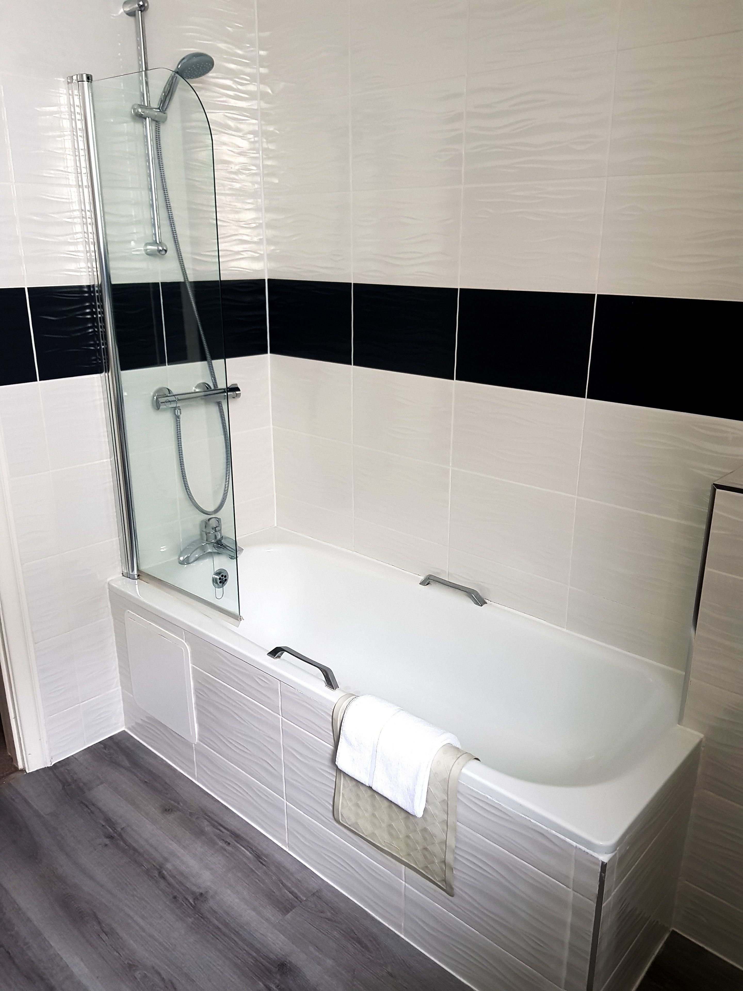 A modern bathroom with a glass-enclosed shower, a white bathtub, and a wooden floor.