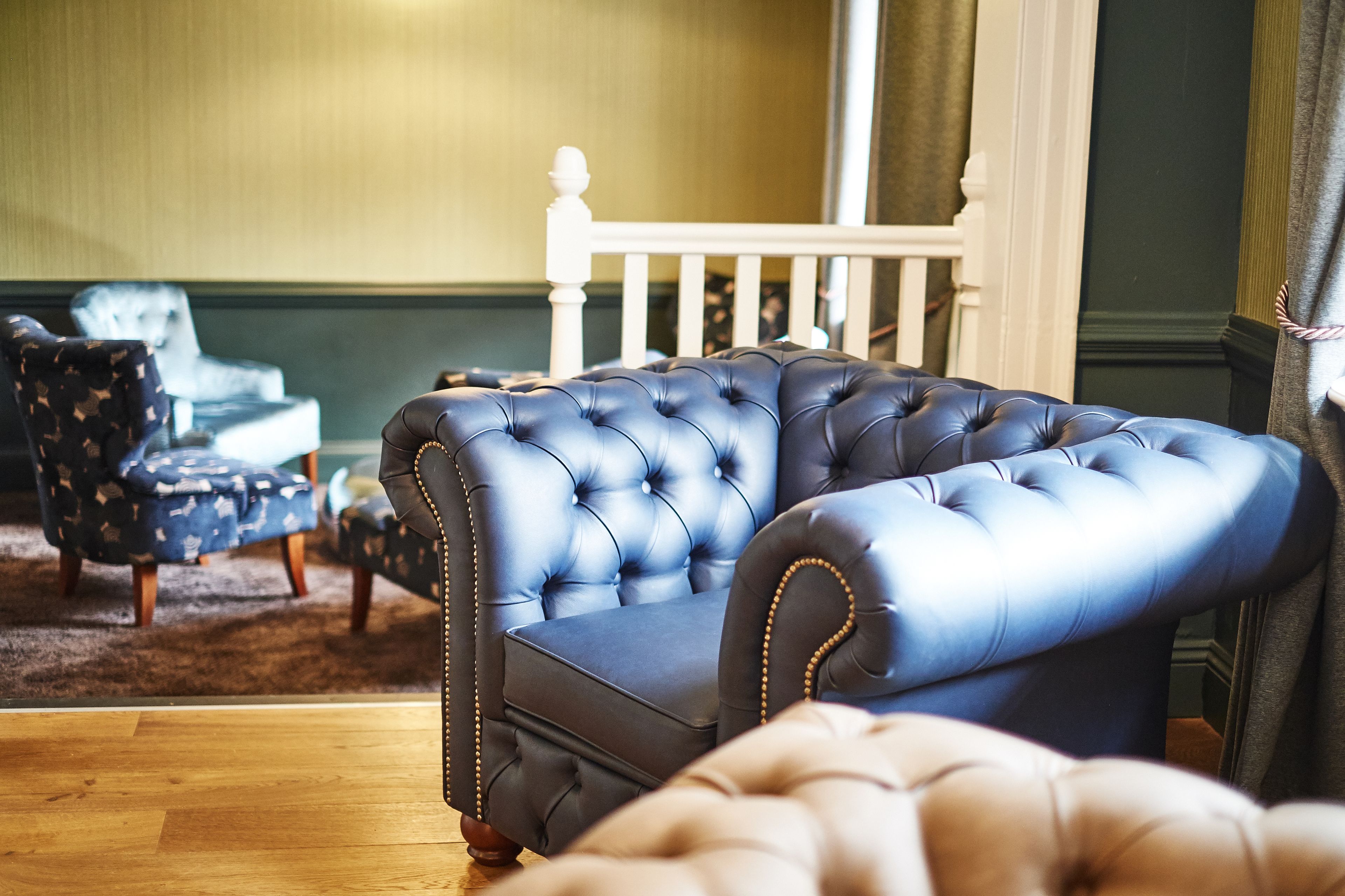A room with a blue tufted sofa, a patterned armchair, and a white chair.