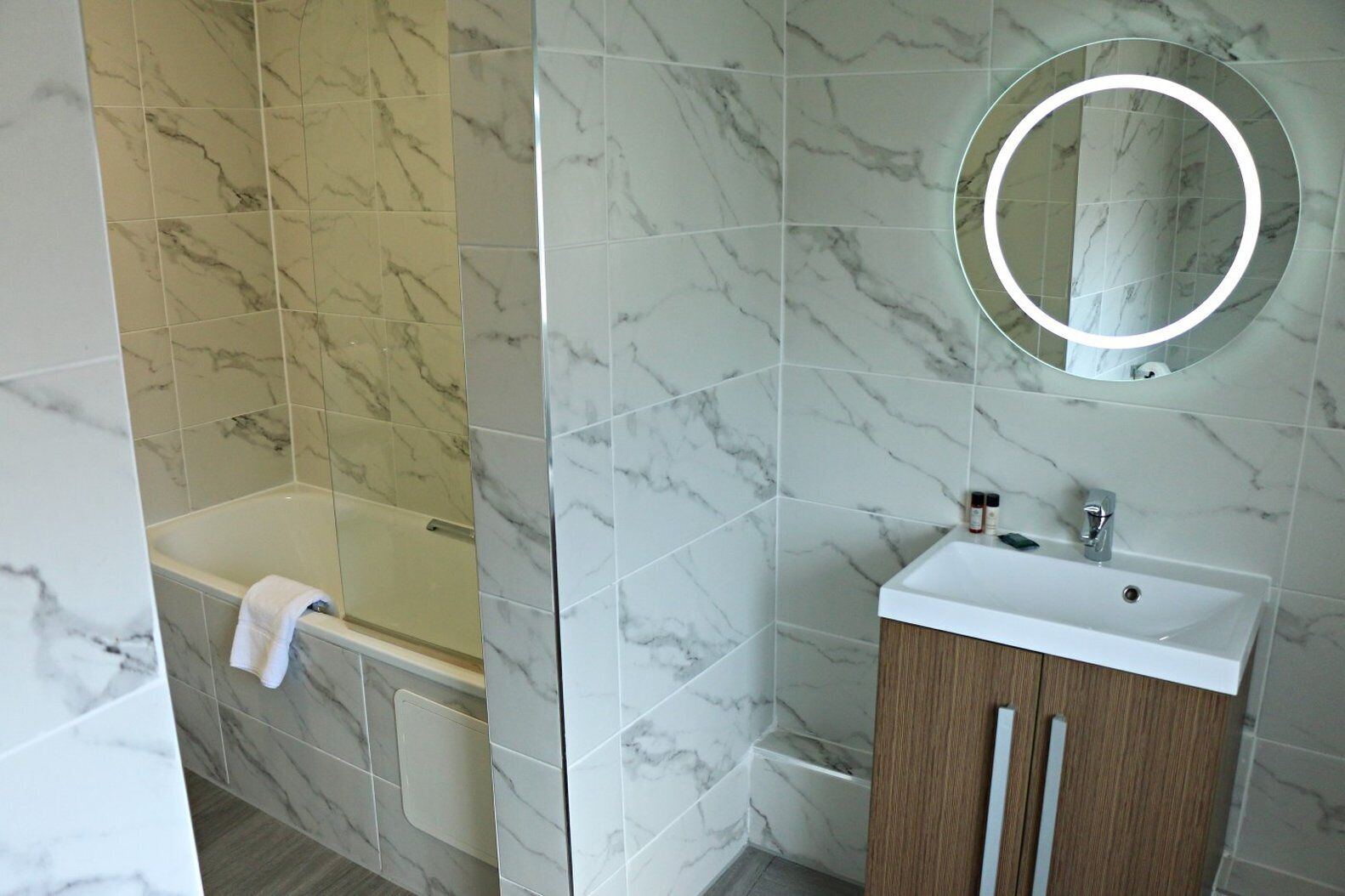 A bathroom with a bathtub, a sink, and a mirror with a light.