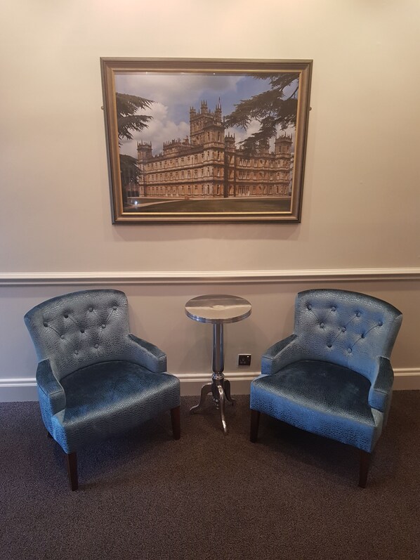 Una habitación con dos sillones tapizados en azul, una mesita redonda y un cuadro colgado en la pared que muestra un castillo.