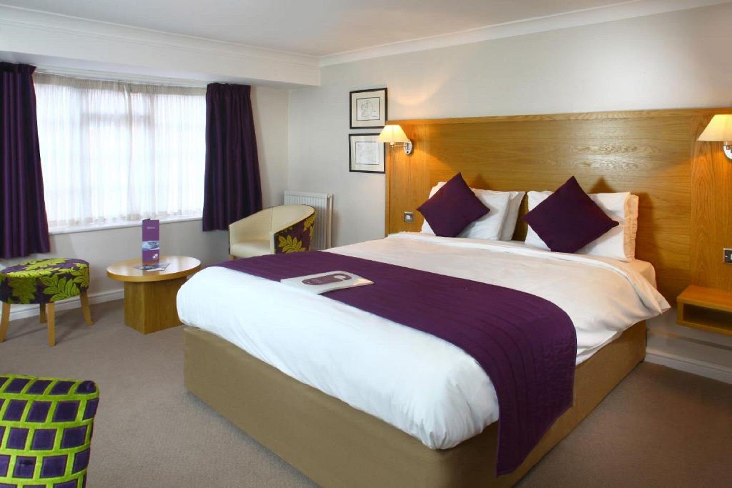 A hotel room with a large bed, a wooden headboard, two bedside tables with lamps, a chair, and a small table.