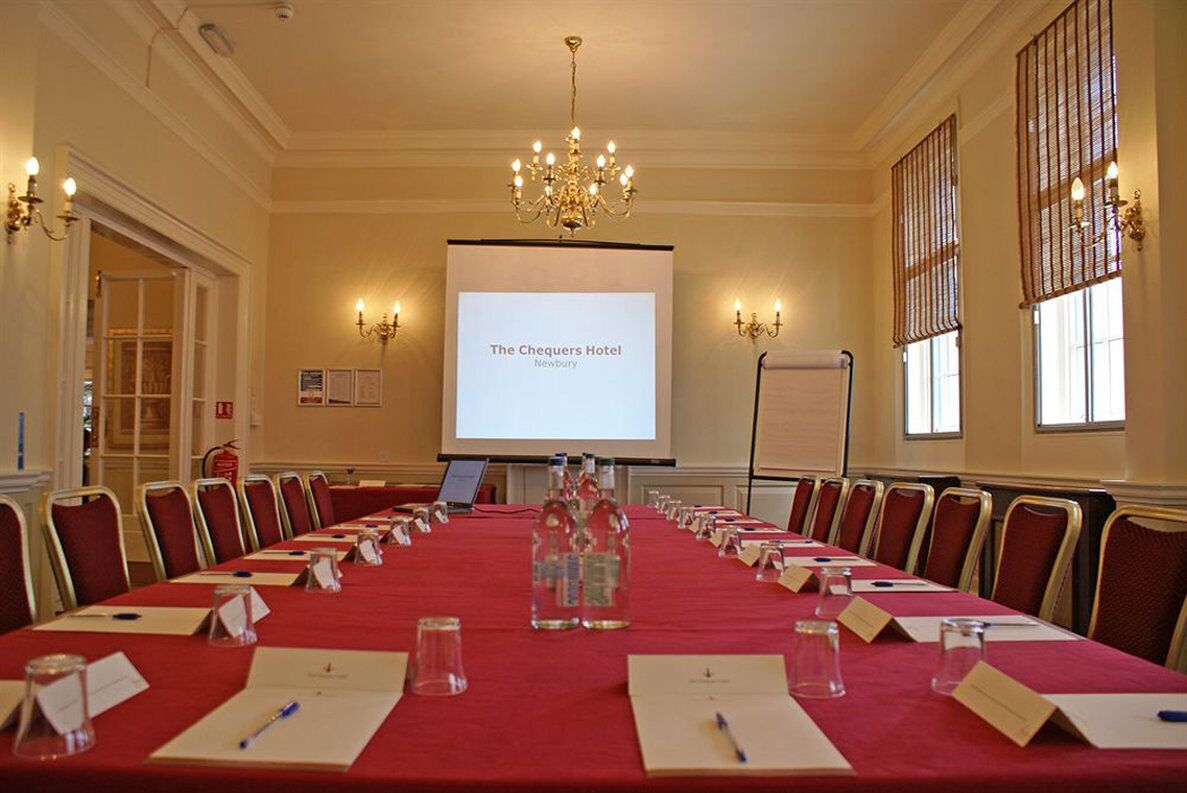 A conference room at The Chequers Hotel with a long table, chairs, name cards, water bottles, and a projector screen displaying the hotel's name.