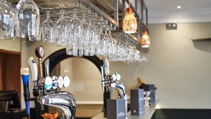 A bar area with multiple taps, glasses hanging above, and a counter with stools. - The Chequers Hotel (Newbury)