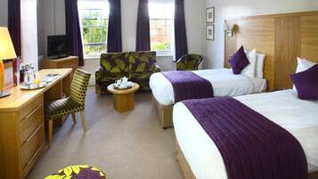 A hotel room with two beds, a desk with a chair, a television, and a window with curtains.