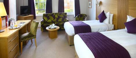 A hotel room with two beds, a desk with a chair, a television, and a window with curtains.
