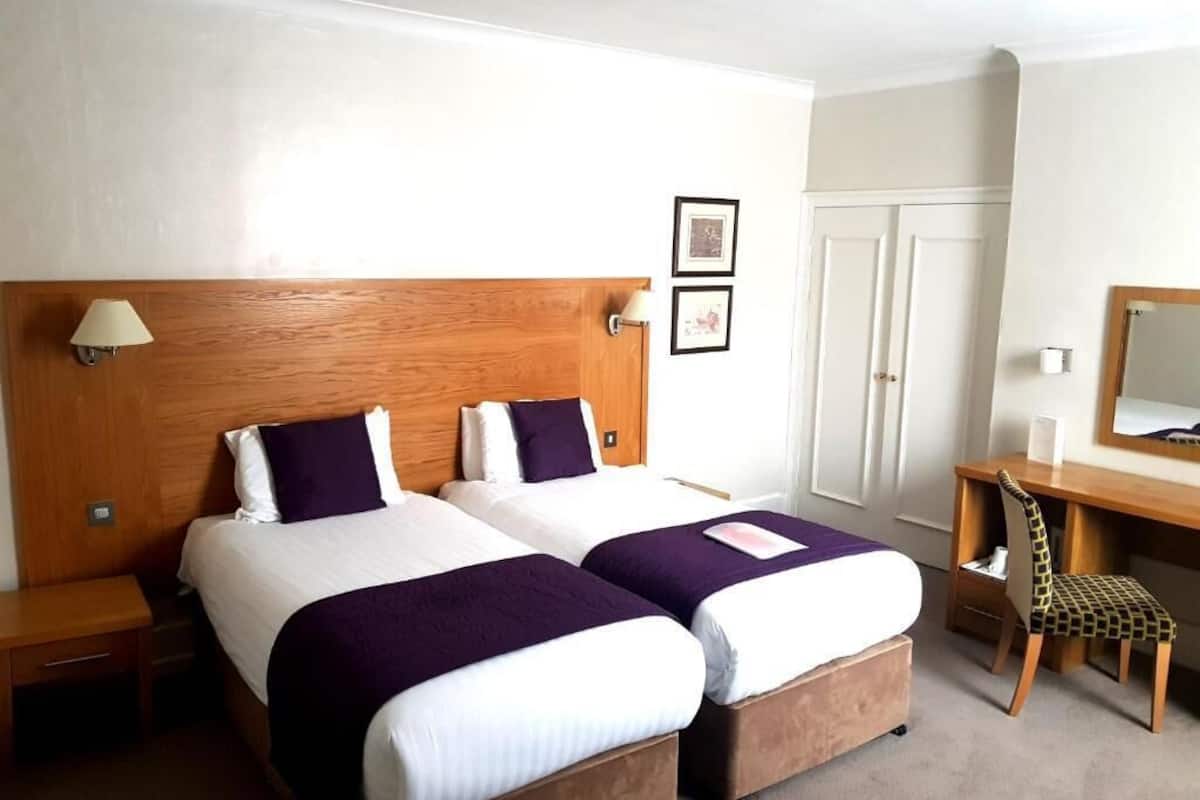 A hotel room with two beds, a desk, a chair, and a wardrobe.