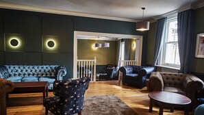 A living room with a blue sofa, a patterned armchair, and a brown sofa. There is a wooden coffee table and a rug. - The Chequers Hotel (Newbury)