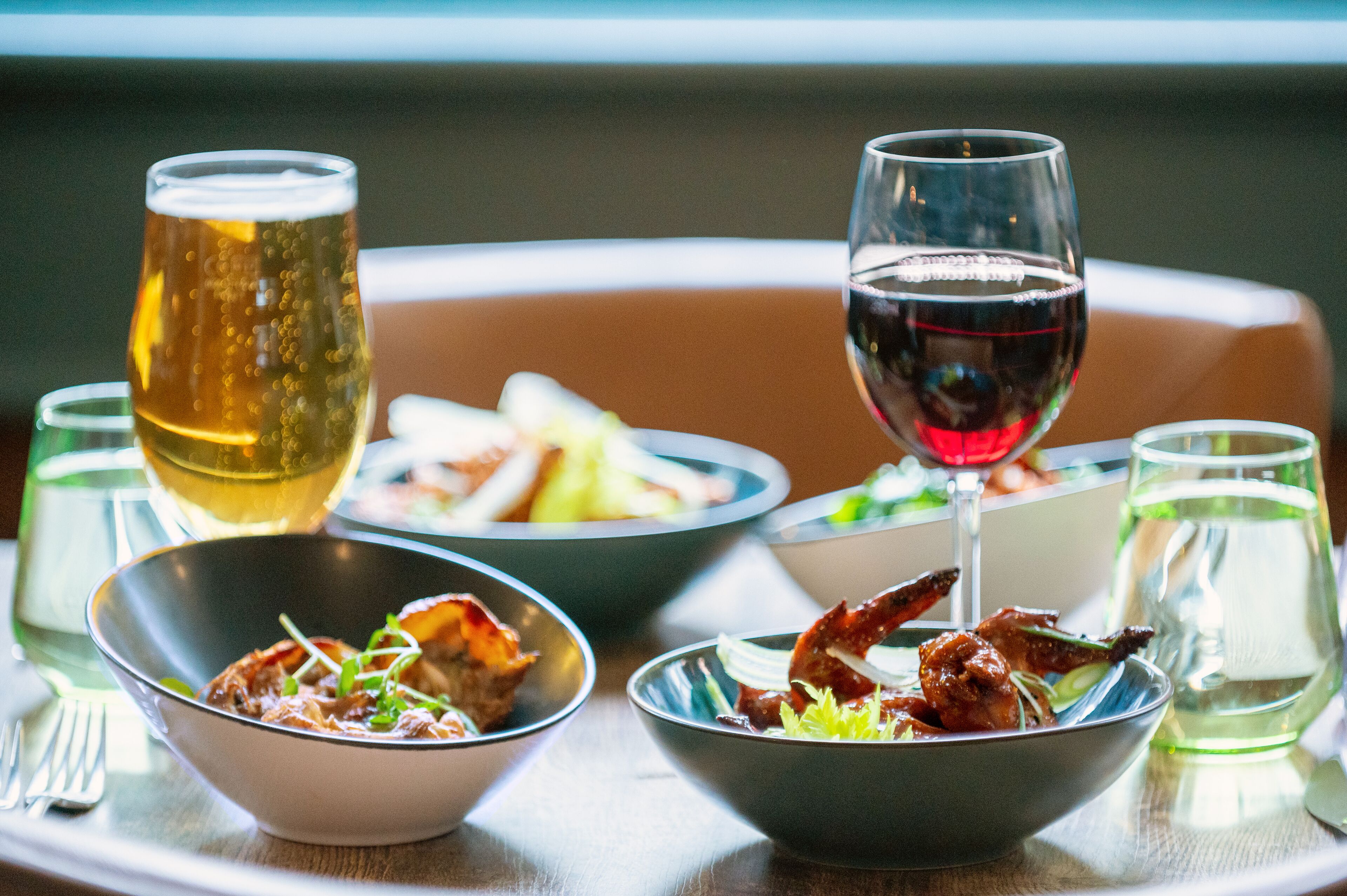A dining table with bowls of food, glasses of beer and wine, and a fork.