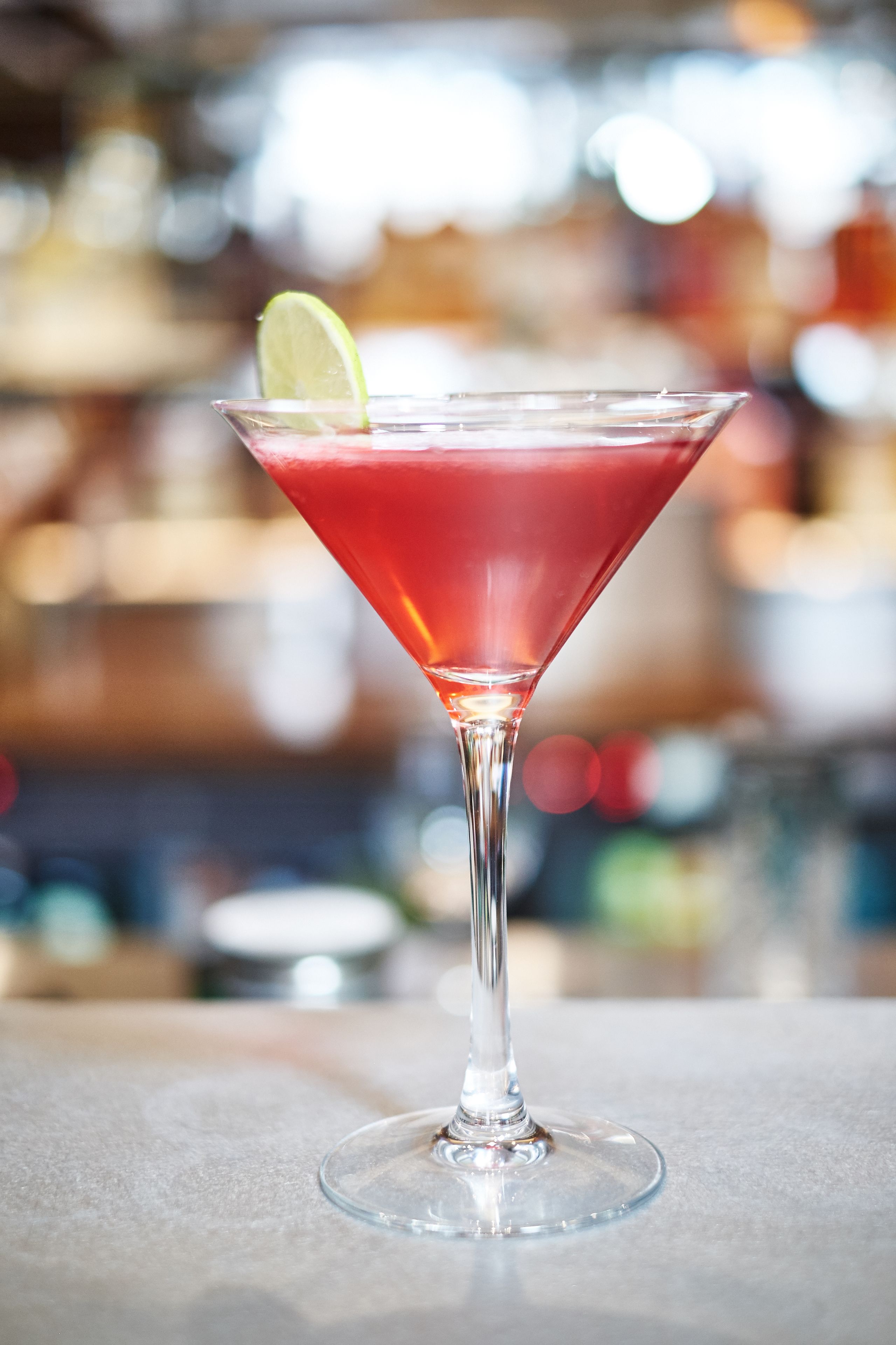 Una copa de martini con un adorno de lima sobre una barra.