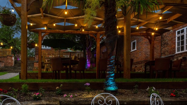 A wooden pergola with string lights, a brick wall, and outdoor seating. - The Chequers Hotel (Newbury)