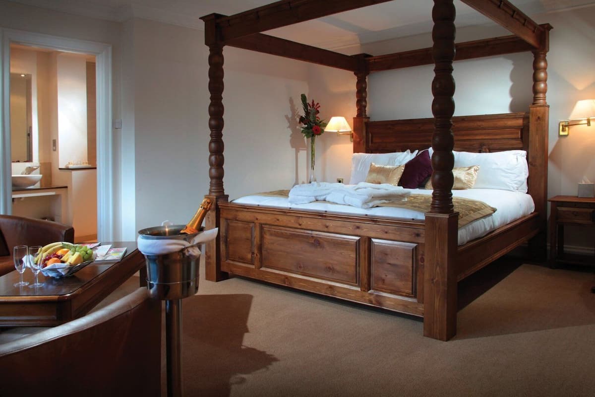 A four-poster bed with a wooden frame and a canopy, a bedside table with a lamp, and a fruit basket on the table.