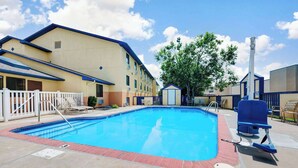 A swimming pool with a brick border, lounge chairs, and a building with a blue roof and beige walls.