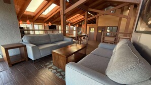 A spacious living area with a high ceiling, wooden beams, and a sofa set.