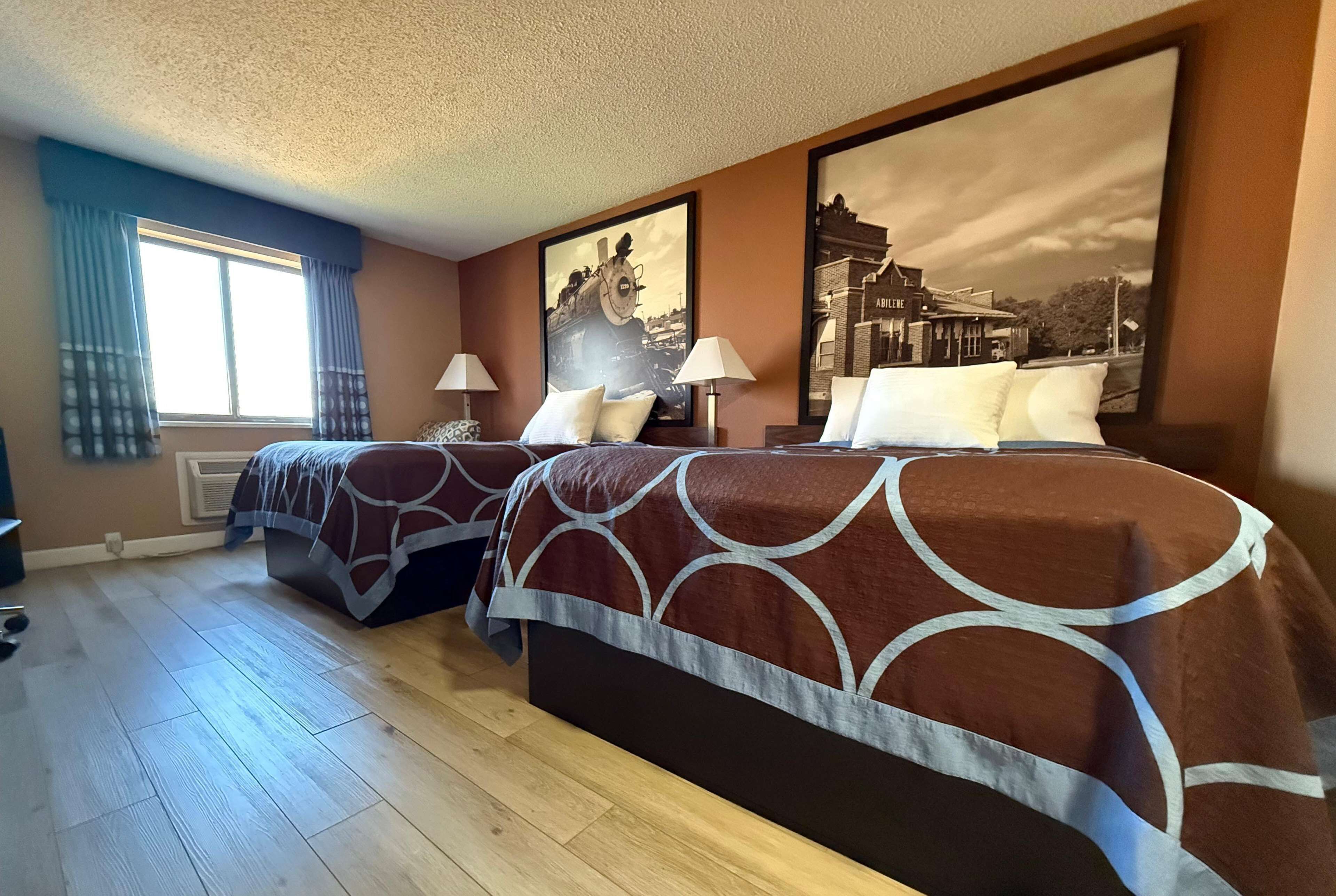 Ein Hotelzimmer mit zwei Betten, einem großen Fenster mit Vorhängen und zwei gerahmten Bildern an der Wand.