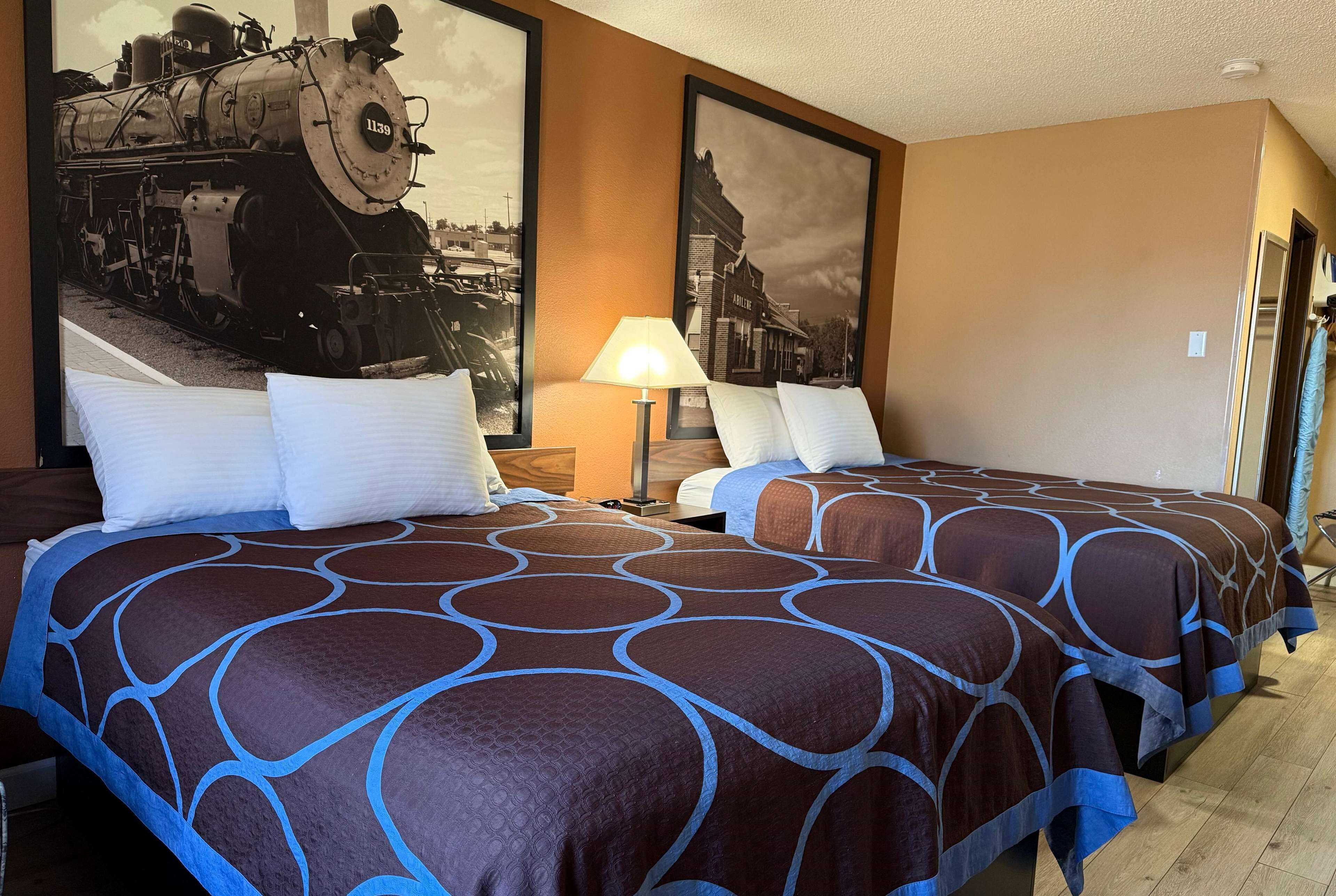 A hotel room with two beds, a large framed picture of a train, and a lamp.