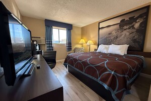 Habitación de hotel con cama, televisor, escritorio, cafetera y ventana con cortinas.