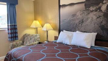 Habitación de hotel con una cama grande, dos lámparas, un sillón estampado y un cuadro grande en la pared.