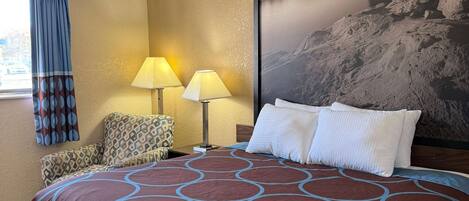 Habitación de hotel con una cama grande, dos lámparas, un sillón estampado y un cuadro grande en la pared.