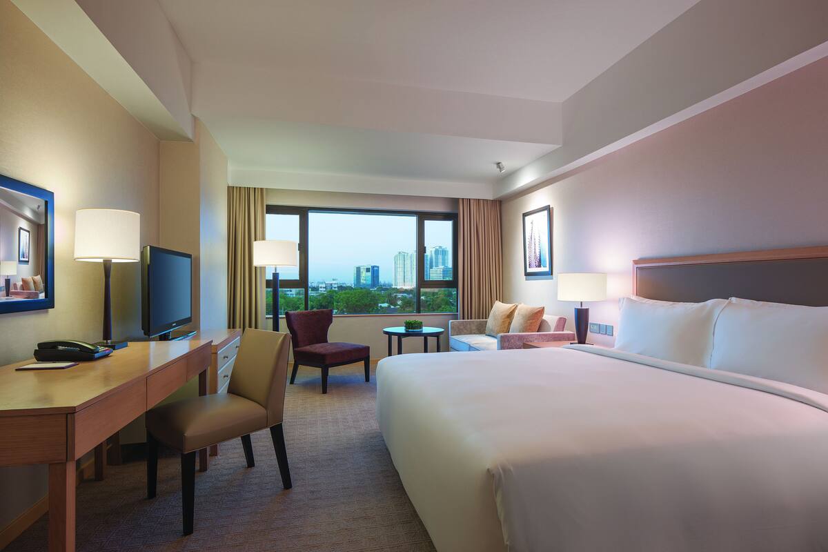 Habitación de hotel con cama, escritorio, silla, televisor y ventana con vista a la ciudad.