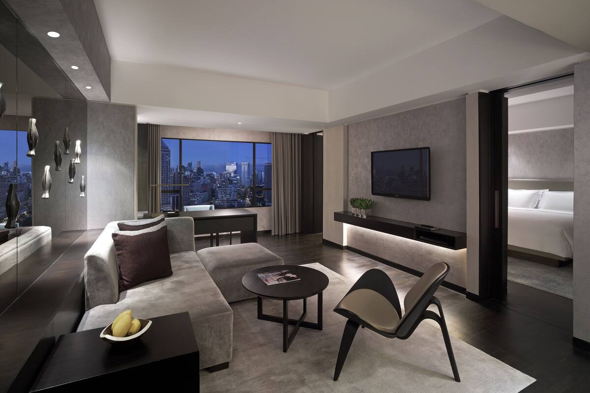 Una habitación de hotel moderna con vistas a la ciudad, una cama grande, una zona de estar con una mesa de centro y un televisor montado en la pared.